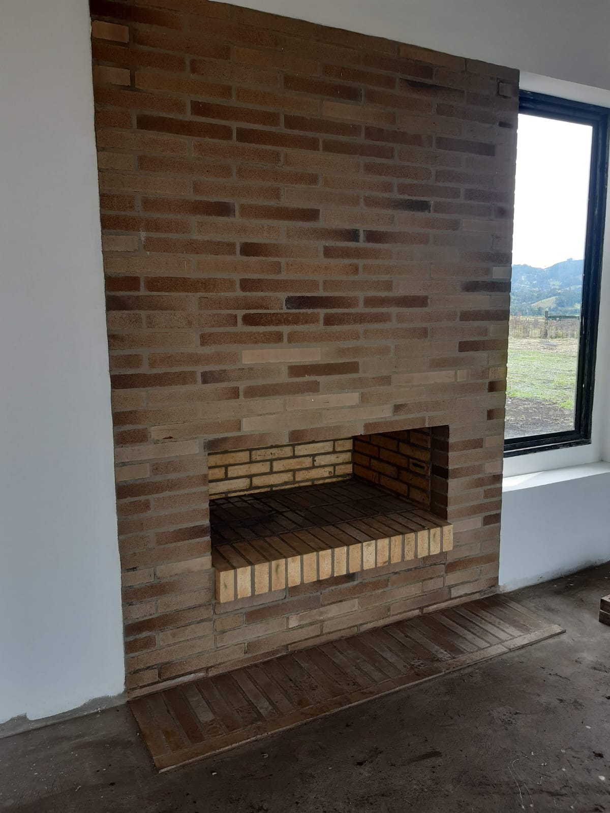 Chimenea de leña en muro de ladrillo a la vista con ventanal